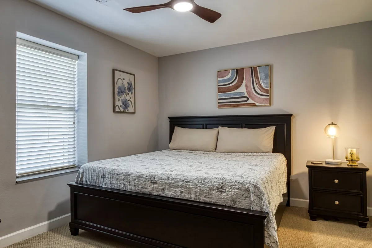 A serene bedroom scene with a cozy bed, nightstand, a window letting in natural light, and tasteful wall art. The clean lines and soft ambiance create a welcoming space for relaxation and rejuvenation.
