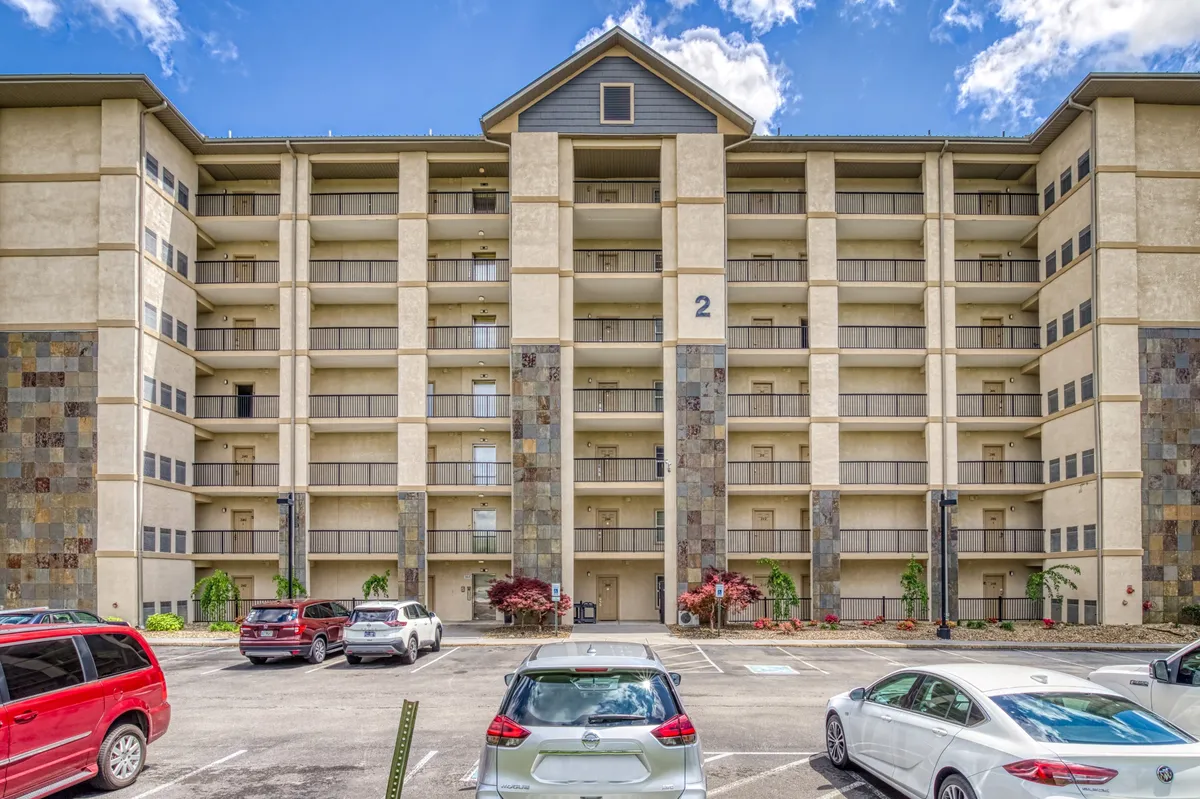 This exterior image features the condo building’s facade with upper balconies, a welcoming parking area, and attractive landscaping. There are visual cues of possible outdoor gatherings, and the setting hints at easy access to nearby attractions.