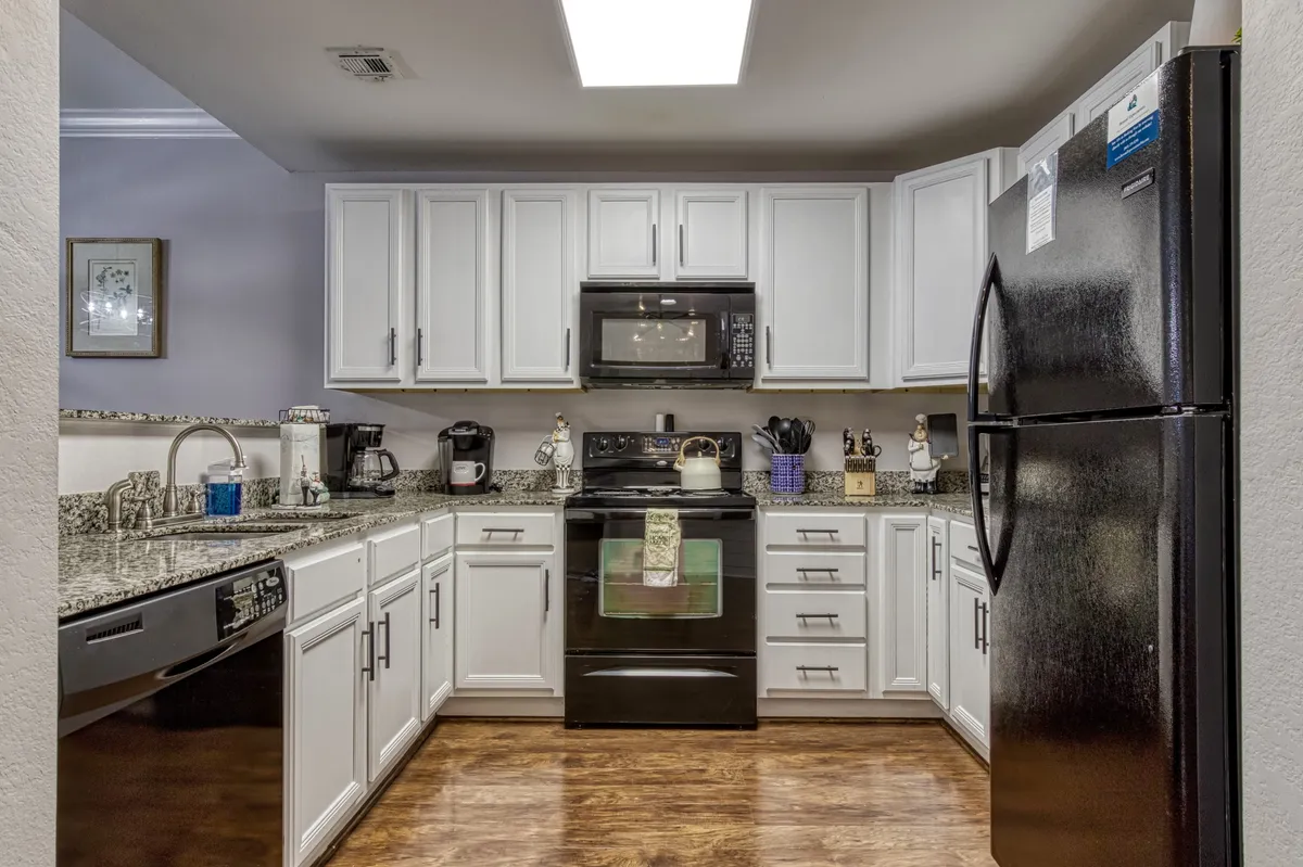 A welcoming kitchen scene showing granite countertops, modern black appliances, white cabinetry, and elegant decorative touches on the counters. The layout encourages cooking, baking, and gathering with family or friends for a shared meal or celebration.