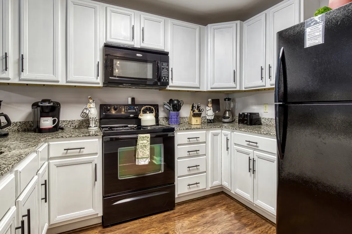 A bright, inviting kitchen featuring sleek black appliances, spacious granite countertops, and crisp white cabinets. Kitchen utensils are neatly arranged, and the space is clearly designed for both everyday meals and special occasions. The overall look is clean, modern, and highly functional, reflecting an atmosphere where cooking is enjoyable and social.
