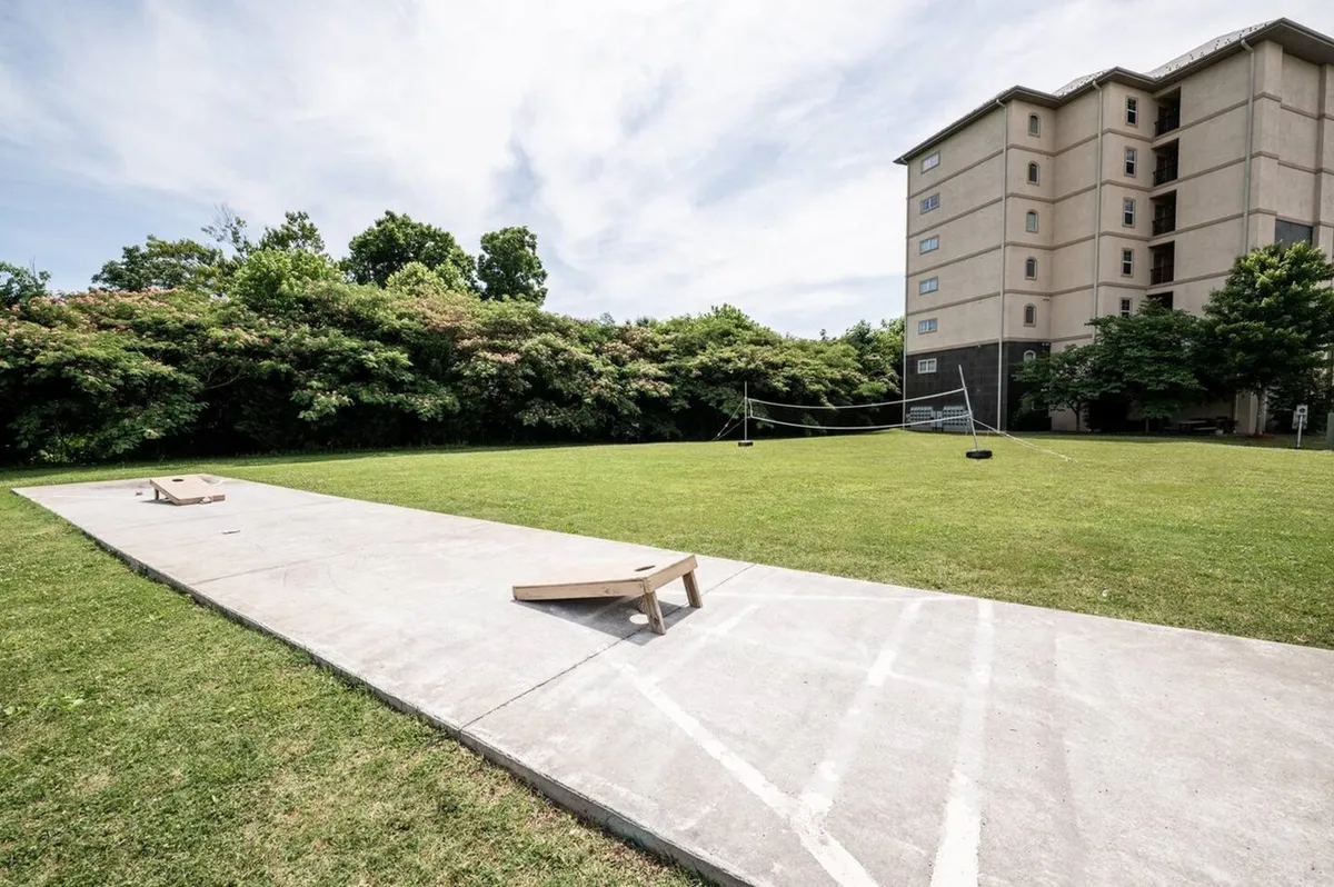 An inviting outdoor recreation area with cornhole boards, a volleyball net, and lush greenery in front of the building. Groups are engaged in lawn games, creating a playful, relaxed environment ideal for families.