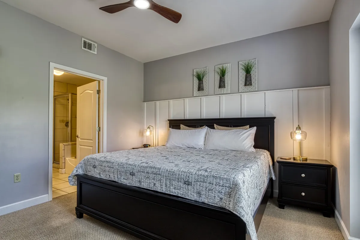A spacious bedroom featuring a large, inviting bed with plush bedding, flanked by matching nightstands and tasteful wall decor. The room includes a direct view of the bathroom entrance, creating a sense of luxury and privacy. Soft lighting and a serene color palette enhance the restful ambiance.