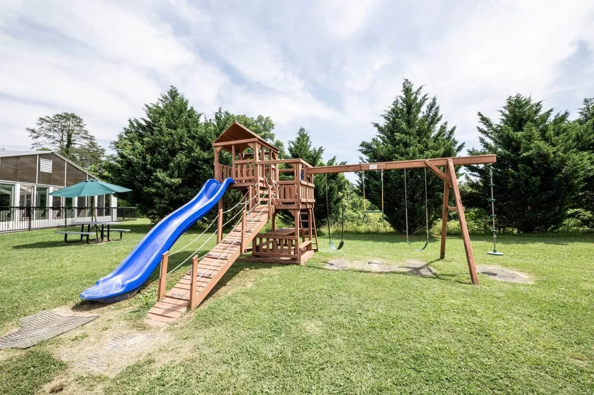 A bright, cheerful playground with a blue slide and swing set sits surrounded by green lawns. Children are shown playing and laughing, while adults supervise nearby, illustrating on-site opportunities for active family fun.