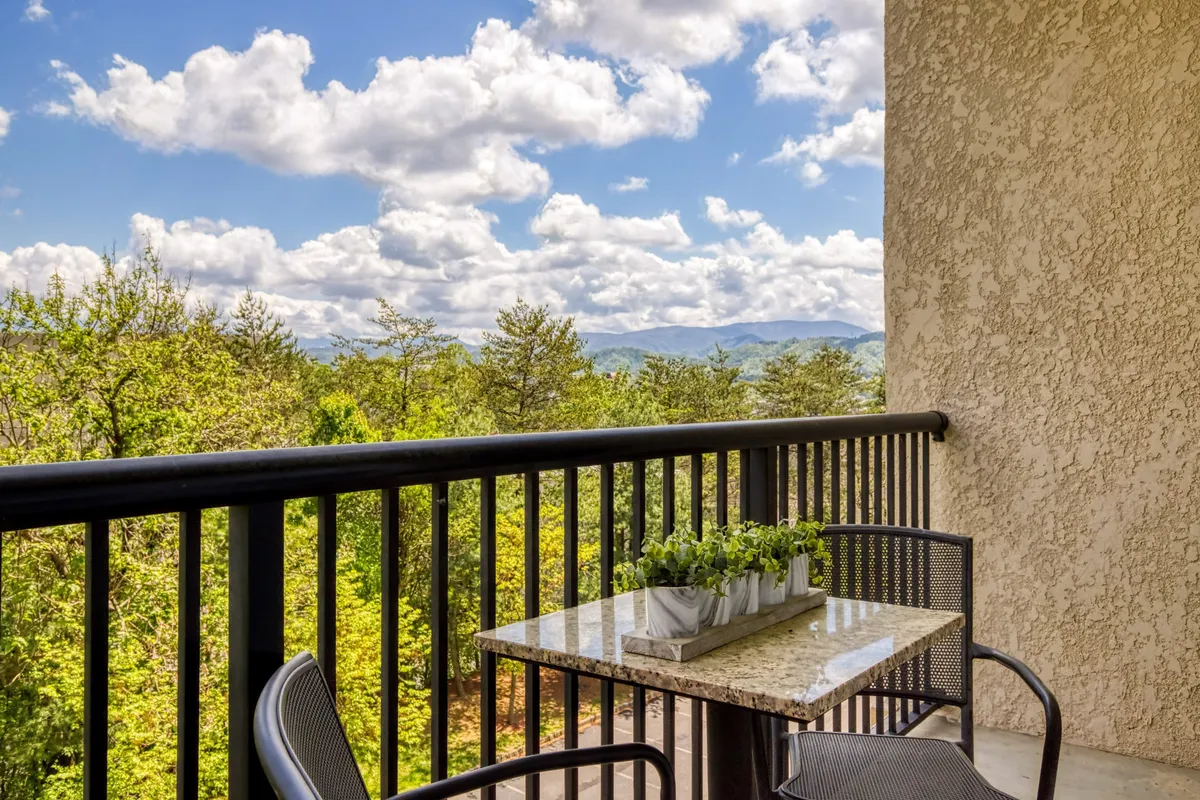 This image captures a private balcony furnished with a table and potted plants, set against a stunning backdrop of mountain views. The scene is tranquil, ideal for enjoying a morning coffee or soaking in natural beauty.