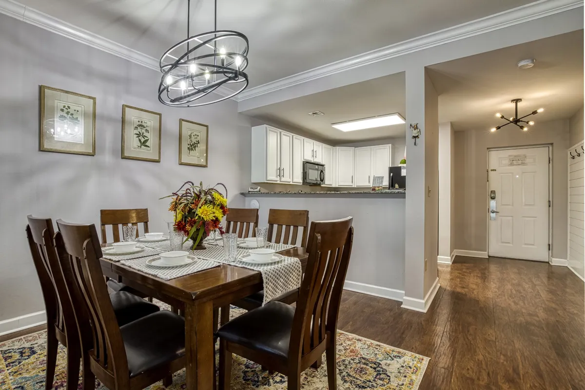 A warm dining area with a wooden dining table set beneath a chandelier, artfully framed by the kitchen entrance and decorative artwork on the walls. The setup suggests intimate meals, family celebrations, or festive brunches, making it perfect for social gatherings.